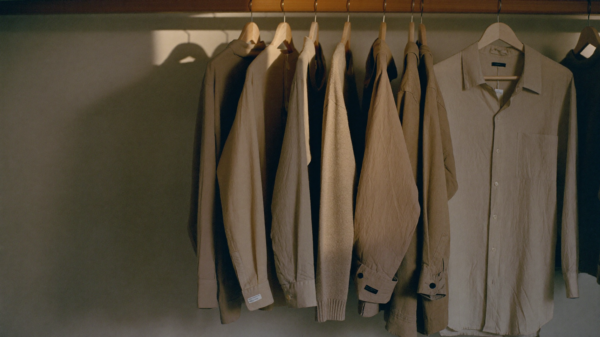A private dressing room, plain garments on bare wooden hangers in soft daylight